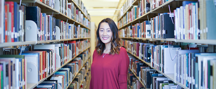 Student standing in rows of books at the library