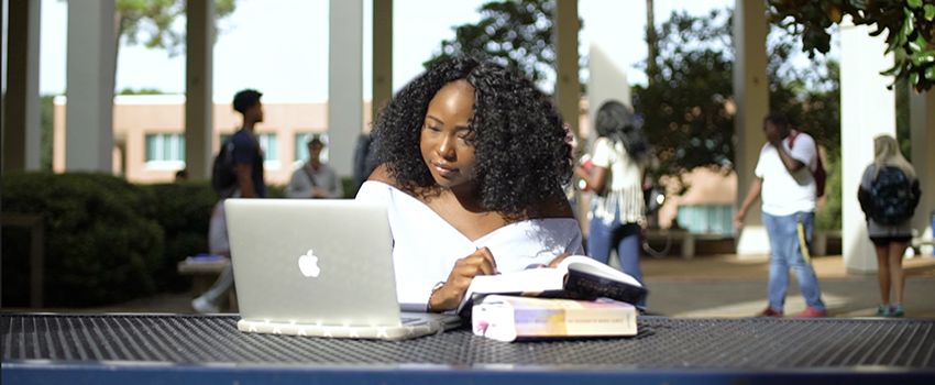 Female studying laptop outside of Humanities building.