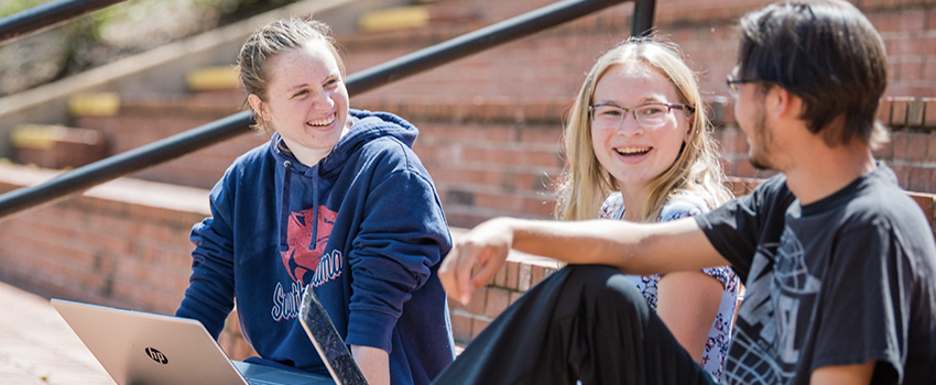 Two female and one male student sitting on the amphitheater steps on campus.