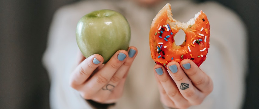 Una mujer sostiene una rosquilla y una manzana en sus manos. 