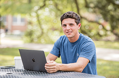 Student working on laptop sitting outside.