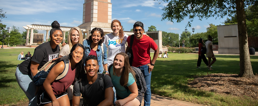 A group of diverse students standing on campus in front of Moulton Tower.