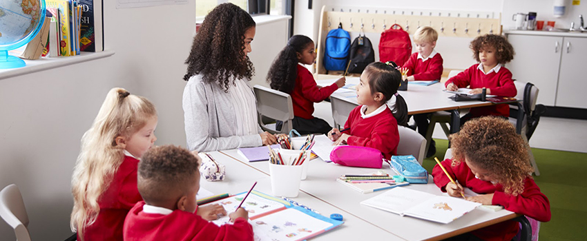 Teacher sitting at table talking to elementary students.