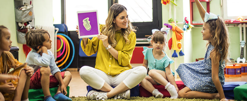 Teacher holding up book while kids sit on carpet in a circle.