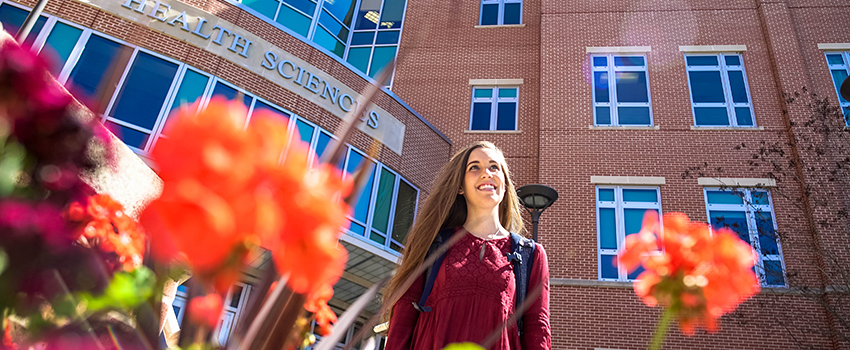 Female student walking out of Allied Health building smiling