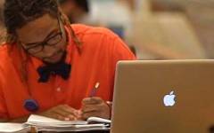 Student writing at desk with laptop.