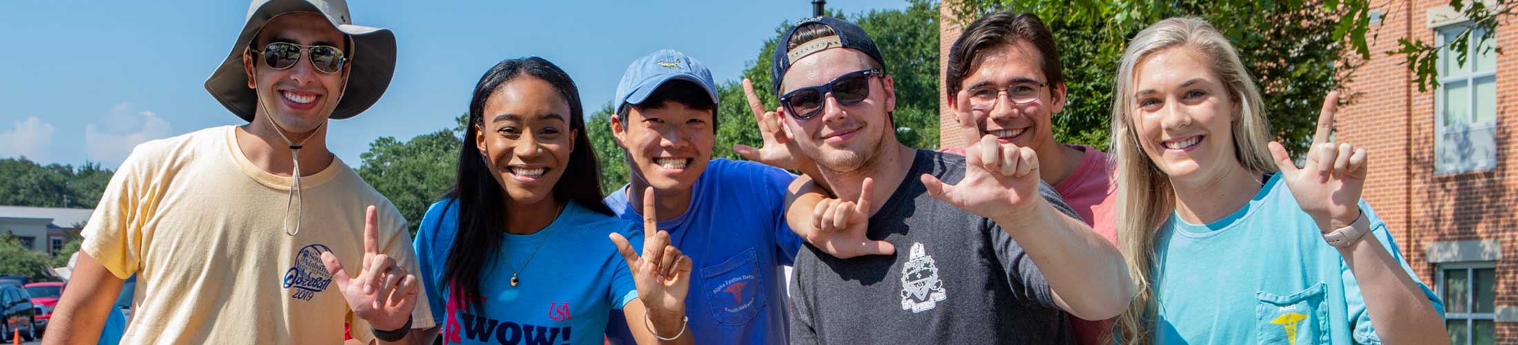 Six students holding up the J sign outside on campus.