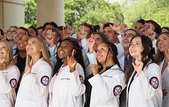 College of Medicine students in white coats holding up J hand.