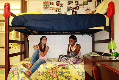 Two female students sitting on bed in dorm