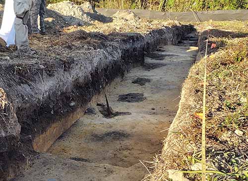 Trench excavation with a line of post holes (the round, dark soil spots). 